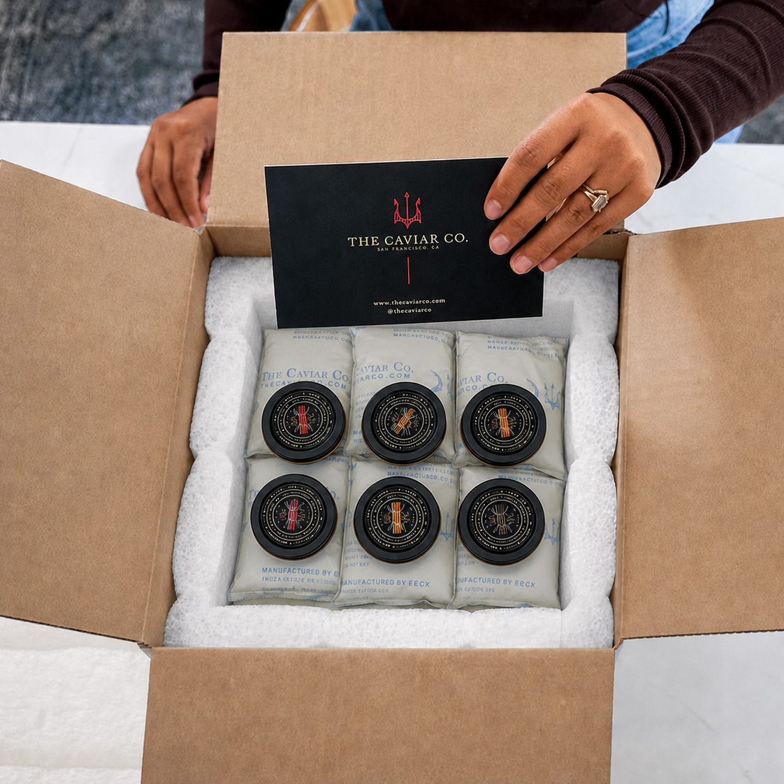 Hands holding a brand card above a specialty shipping box packed with caviar tins and custom Cold Ice gel packs.
