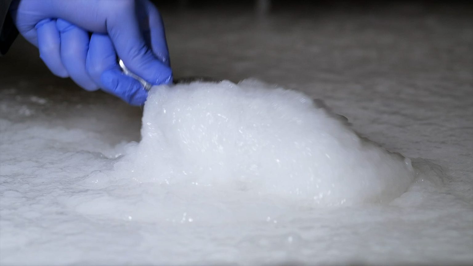 A gloved hand scooping or mixing a thick white foam refrigerant gel material.